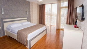 A hotel room with a bed, a bedside table, a mirror, and a window with curtains. - Rio Batumi (Batumi)