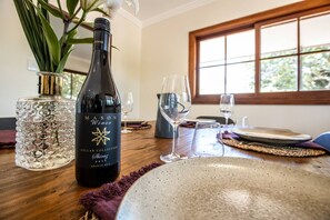 A dining table with a bottle of Mason Wines Shiraz 2016, a glass vase with a plant, and a window with a view of trees. - Administration House Winery Stay (Tamborine Mountain)
