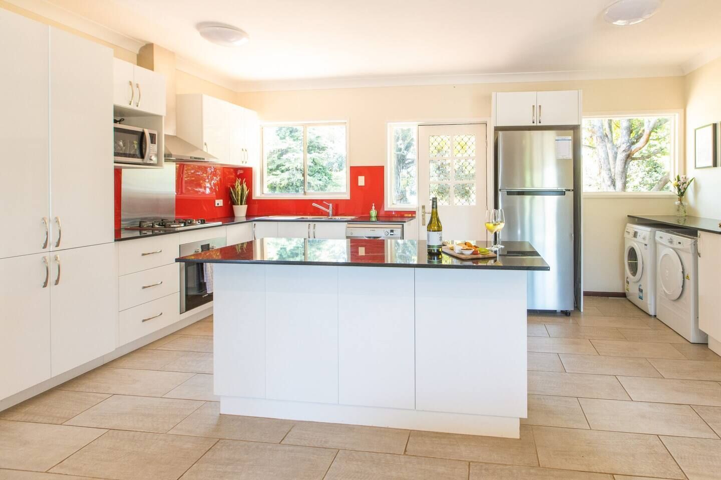 A modern kitchen with white cabinetry, a central island, a stainless steel refrigerator, and a washing machine.