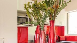 Cuina amb armaris blancs, tauleig vermell i dos vasos vermells amb plantes.