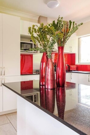 A kitchen with white cabinets, a red countertop, and two red vases with plants.