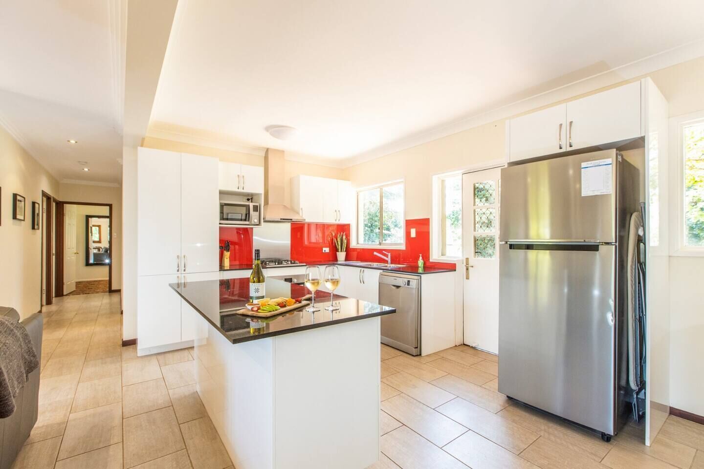 A modern kitchen with a central island, stainless steel appliances, and a red backsplash.