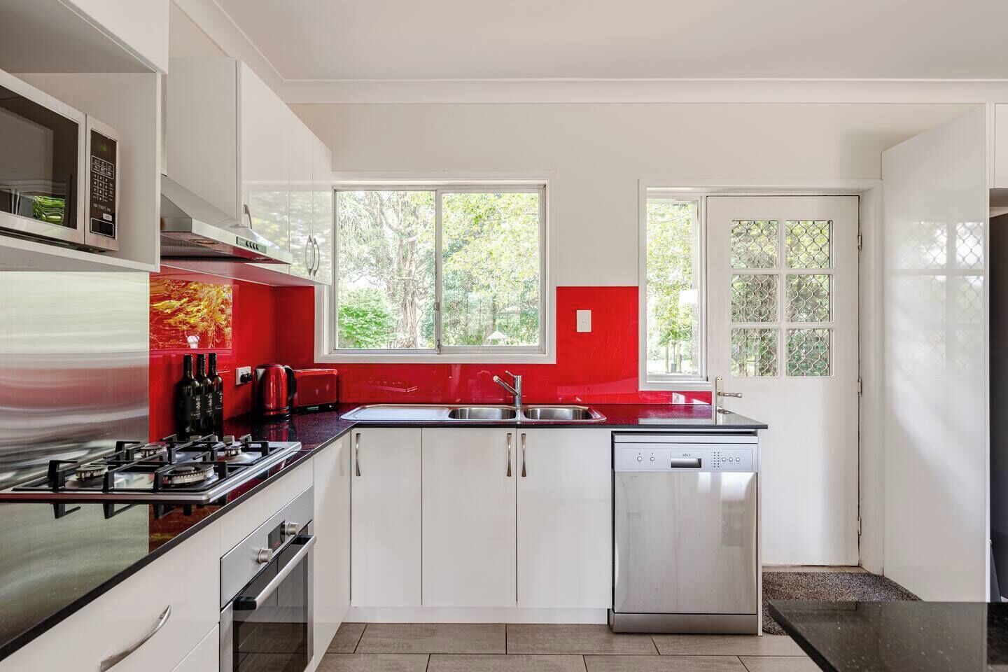 A modern kitchen with white cabinets, a red backsplash, a stainless steel range, and a dishwasher.