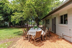 An outdoor patio with a table set for dining, surrounded by chairs, and a building with windows and a door. - Administration House Winery Stay (Tamborine Mountain)