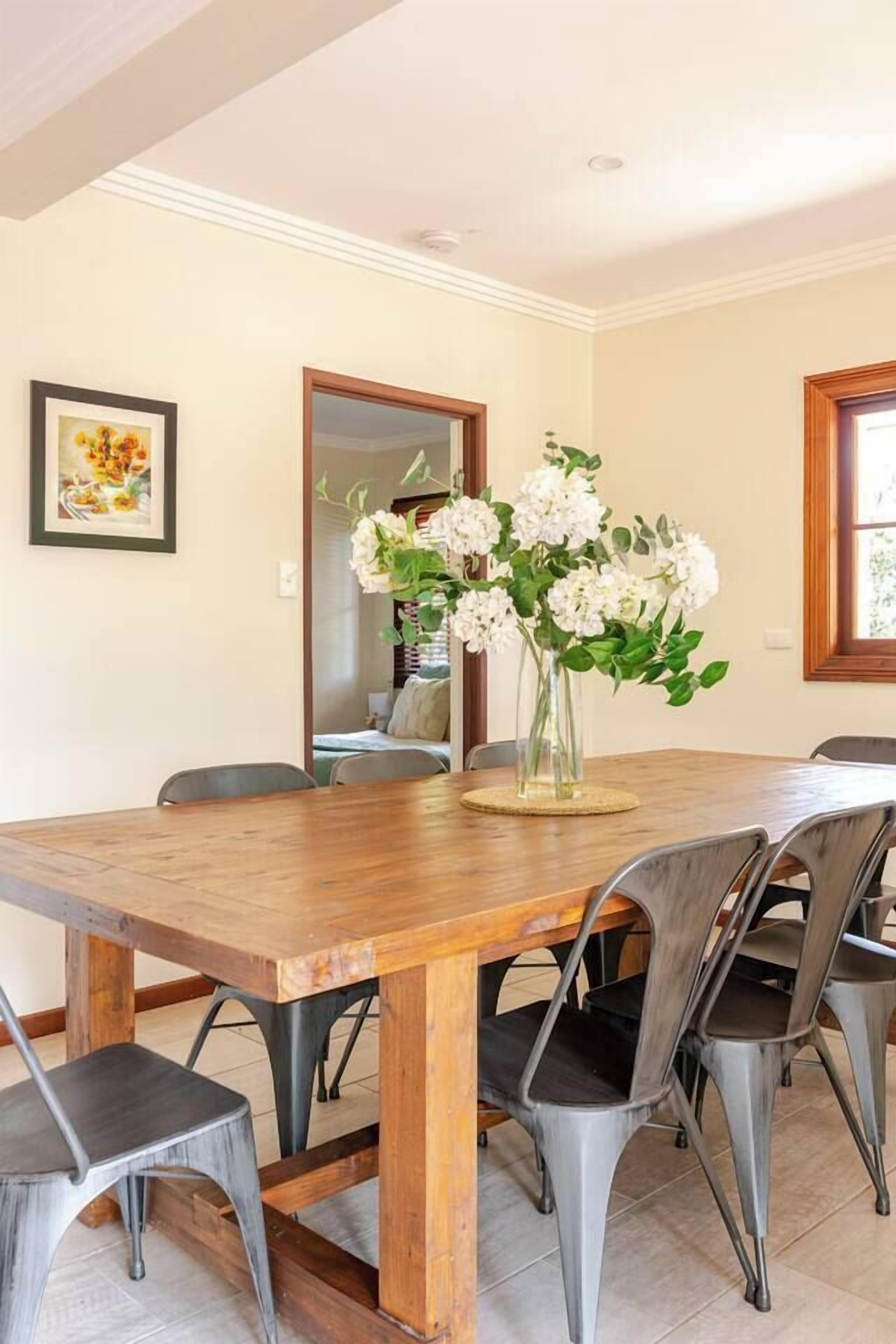 Ein Essbereich mit Holztisch, Metallstühlen, einer Blumenvase und einem gerahmten Bild an der Wand.