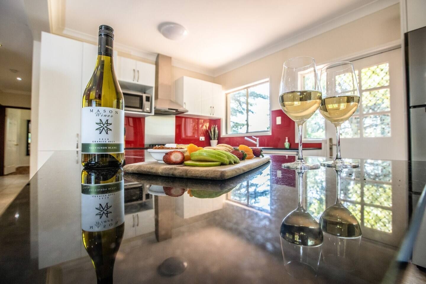A kitchen with a wine bottle and glasses on the counter, a fruit platter, and a modern design.