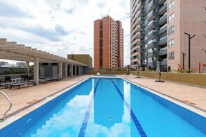 A swimming pool with a pergola and lounge chairs, surrounded by high-rise buildings. - lEPl Modern Loft in El Poblado W/pool & Gym (Medellín)