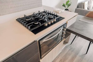 A modern kitchen with a built-in gas stove, oven, and a dining area with a table and chairs. - lEPl Modern Loft in El Poblado W/pool & Gym (Medellín)