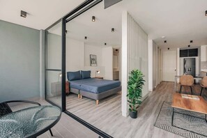Ein modernes Schlafzimmer mit Bett, Nachttisch, Lampe und Blick durch eine Glastür in einen anderen Raum.