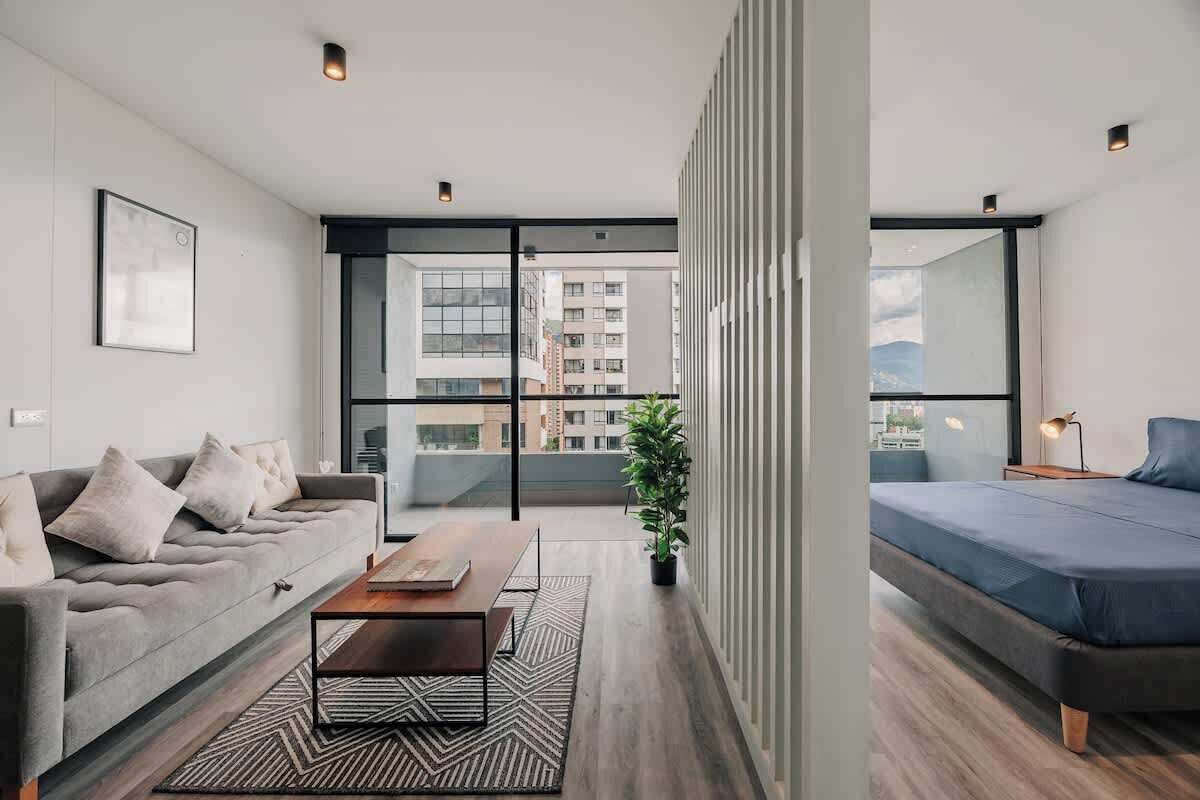 Un salon moderne avec un canapé, une table basse et un lit. Une grande fenêtre offre une vue sur les bâtiments à l’extérieur.
