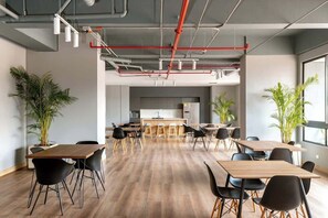 A modern office space with multiple tables and chairs, a kitchen area in the background, and large windows allowing natural light. - lEPl Modern Loft in El Poblado W/pool & Gym (Medellín)
