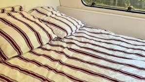 Cama com roupa de cama listrada dentro de um veículo.