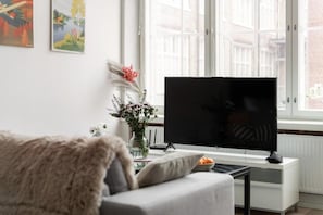 A living room with a flat-screen TV, a sofa, a coffee table, and a window with a view of buildings. - Värjäri - City apartments by Comein (Tampere)