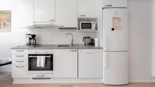Uma cozinha moderna com armários brancos, forno embutido, micro-ondas e geladeira.