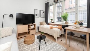 Quarto moderno e bem iluminado, com uma cama, televisão, escrivaninha e janela com vista para edifícios.