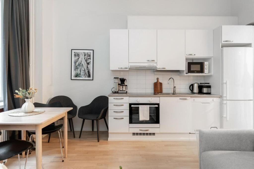 A modern kitchen with white cabinets, a microwave, an oven, and a dining area with a table and chairs.