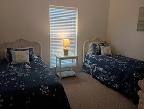 A bedroom with two beds, a nightstand, and a window with blinds. - Seascape Escape 304 (South Padre Island)