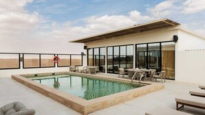 Ein Poolbereich auf dem Dach mit Pool, Liegestühlen und einem Gebäude mit großen Fenstern.