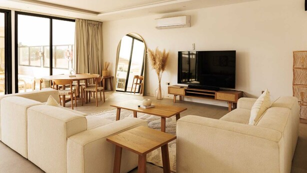 Ein modernes Wohnzimmer mit einer Sofagarnitur, einem Couchtisch, einem Fernseher und einem Essbereich mit Stühlen und einem Tisch.
