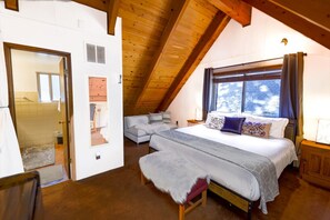 A bedroom with a sloped ceiling, a bed with a white bedspread, a bench, and a window with curtains. - Chairlift Cabin Near Snow Summit w Loft & Fireplace (Big Bear Lake)