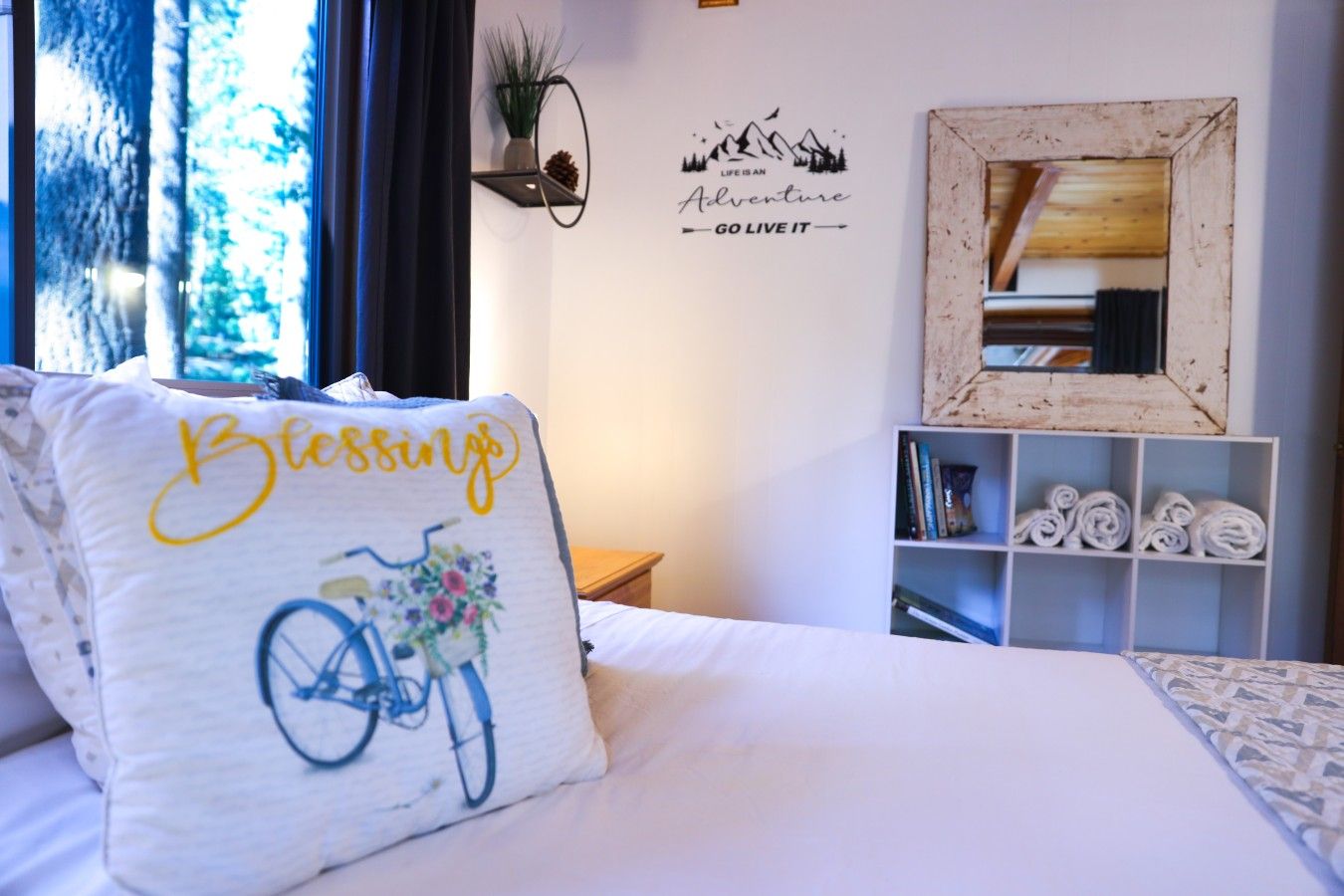 A neatly made bed with a pillow featuring a bicycle and the word 'Blessings'.