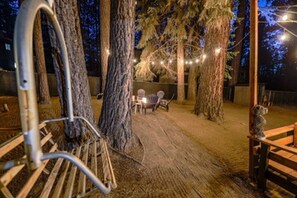 Ein rustikaler Außenbereich mit Holzbänken und -stühlen, umgeben von Bäumen und Lichterketten.