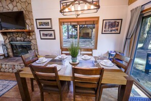 A dining area with a stone fireplace, wooden table, and chairs. - Chairlift Cabin Near Snow Summit w Loft & Fireplace (Big Bear Lake)