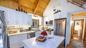 A modern kitchen with white cabinetry, a central island, stainless steel appliances, and a wooden ceiling. - Cozy Cabin Near Snow Summit w Loft & Fireplace (Big Bear Lake)