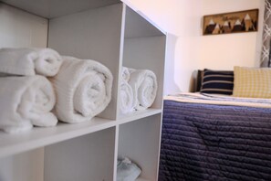 A neatly organized shelf with rolled towels, a bed with a dark quilt and striped pillows, and a wall with a framed picture. - Chairlift Cabin Near Snow Summit w Loft & Fireplace (Big Bear Lake)