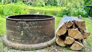 Un contenitore metallico e una pila di legna accanto a un lago, con alberi sullo sfondo.