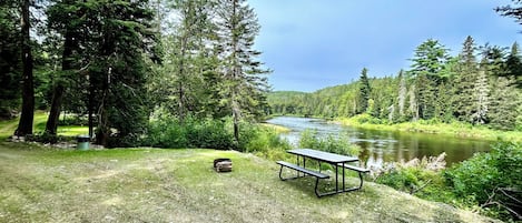 A picnic table and bench by a river in a forested area.