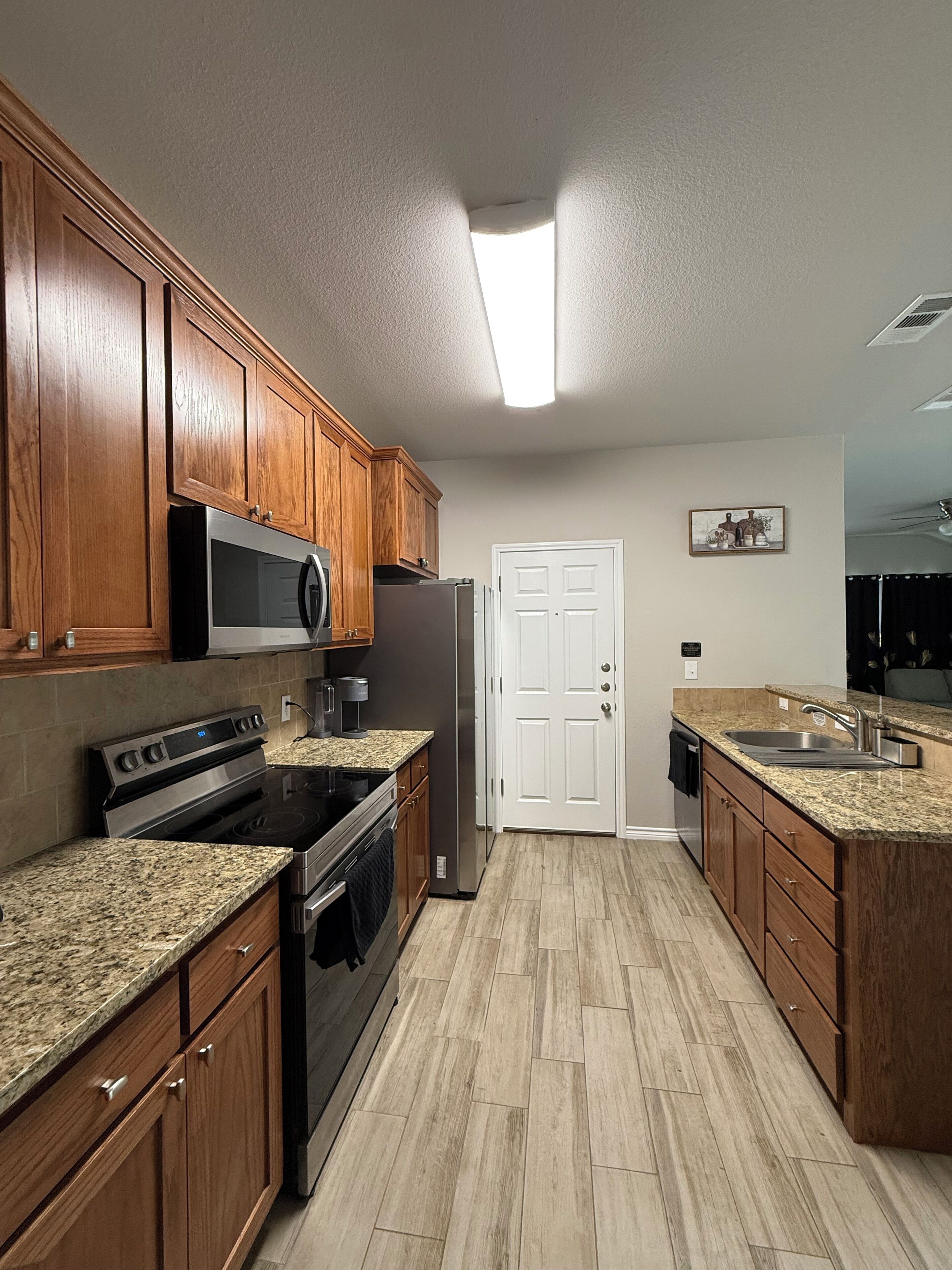 A kitchen with wooden cabinets, stainless steel appliances, granite countertops, and a tiled floor.