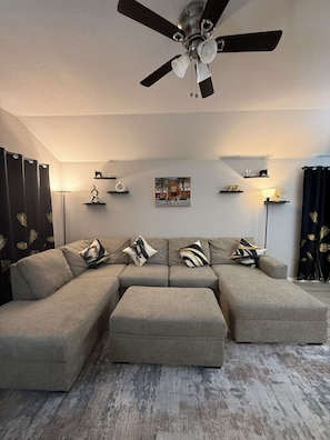 A modern living room with a sectional sofa, a ceiling fan, and decorative wall art.