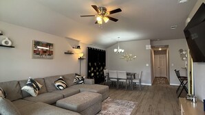 En moderne stue med en hjørnesofa, et spiseområde med en lysekrone og en ventilator i loftet.