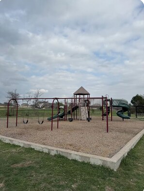 Une aire de jeux avec des balançoires, un toboggan et une structure d’escalade.