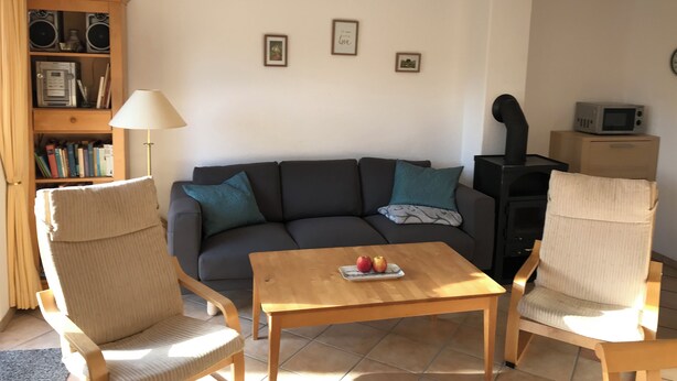 Un salon comprenant un canapé, deux fauteuils, une table basse avec des pommes, une bibliothèque, une lampe et une cheminée.