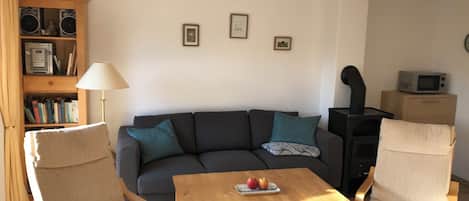 A living room with a sofa, two armchairs, a coffee table with apples, a bookshelf, a lamp, and a fireplace.