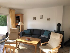 Ein Wohnzimmer mit einer Couch, zwei Sesseln, einem Holztisch, einem Bücherregal und einem Kamin.