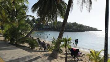 A beach with palm trees, a wooden walkway, and people swimming and relaxing.