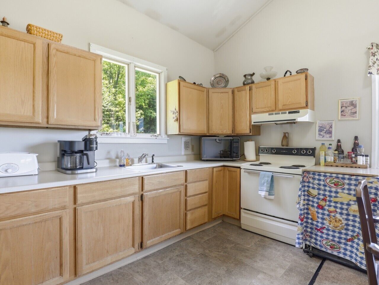 A kitchen with wooden cabinets, a microwave, a coffee maker, and a table with a patterned tablecloth.