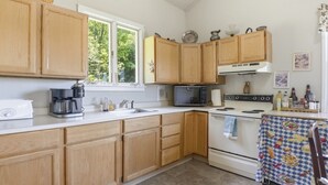 A kitchen with wooden cabinets, a microwave, a coffee maker, and a table with a patterned tablecloth. - Charming Apartment w/ Shared Deck & Lake Views (Lawrenceville)