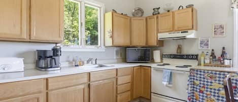 A kitchen with wooden cabinets, a microwave, a coffee maker, and a table with a patterned tablecloth.
