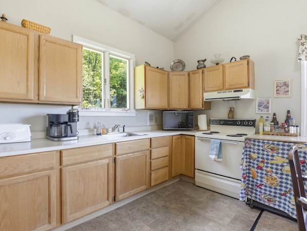 A kitchen with wooden cabinets, a microwave, a coffee maker, and a table with a patterned tablecloth.