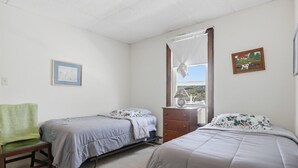 A bedroom with two single beds, a wooden dresser, a chair, and a window with a view. - Charming Apartment w/ Shared Deck & Lake Views (Lawrenceville)