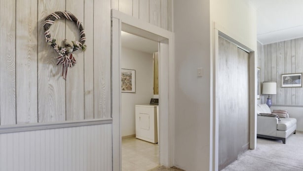 A hallway with a door leading to a laundry room and a living area with a couch and a lamp. - Charming Apartment w/ Shared Deck & Lake Views (Lawrenceville)