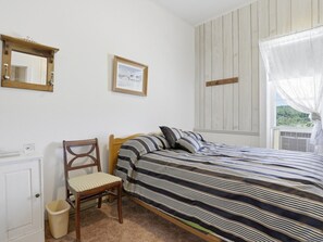 A bedroom with a bed, a chair, a bedside table, a mirror, and a window with a view. - Charming Apartment w/ Shared Deck & Lake Views (Lawrenceville)