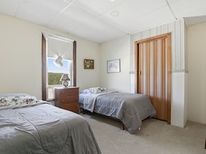 A bedroom with two beds, a dresser, a window with curtains, and a door with vertical blinds.