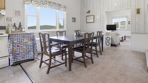 A dining area with a table and chairs, a kitchen area with a stove and refrigerator, and a television in the background. - Charming Apartment w/ Shared Deck & Lake Views (Lawrenceville)