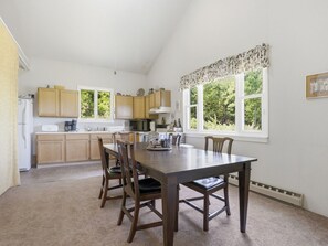 A kitchen with wooden cabinets, a dining table with chairs, and a window with a view of greenery. - Charming Apartment w/ Shared Deck & Lake Views (Lawrenceville)