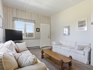 Una sala de estar con un sofá, una mesa de centro de madera, un televisor y una puerta.